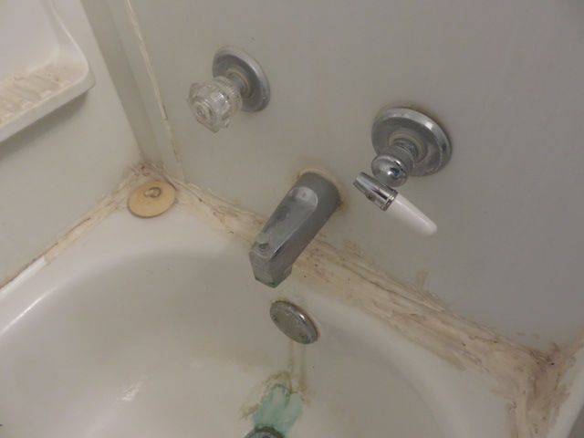 Stained and uneven failed caulk around a bathtub surround